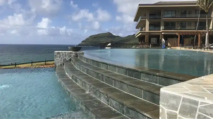Infinity pool stepping down in tiled cascades toward the ocean and a green volcanic headland
