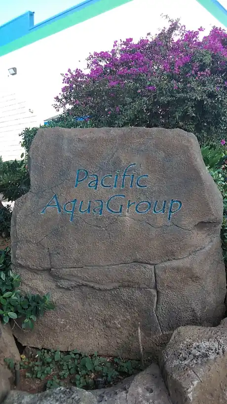 Carved rock sign lettered Pacific AquaGroup with bougainvillea beside it at the Kapolei yard