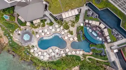 Aerial view of a resort pool deck with two freeform pools, a hexagonal spa and a long lap channel on a rock shoreline
