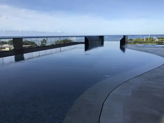 Dark infinity pool edge meeting the ocean horizon under a clear sky at Anaha