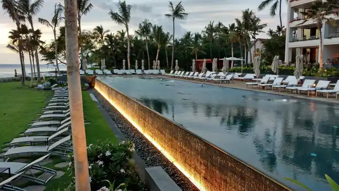 Long lap pool at Four Seasons Ko Olina at dusk, lit coping edge beside a row of loungers