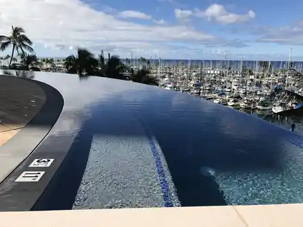Hawaii Prince infinity pool with dark tile and a curved vanishing edge above a marina of yachts