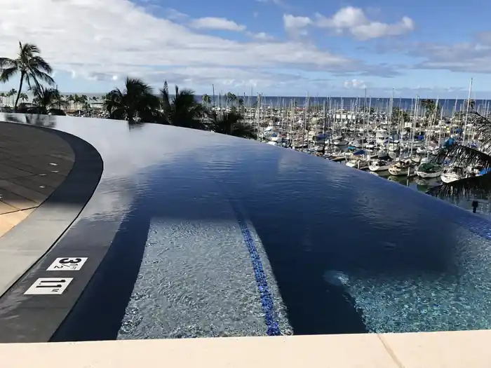 Hawaii Prince infinity pool with dark tile and a curved vanishing edge above a marina of yachts