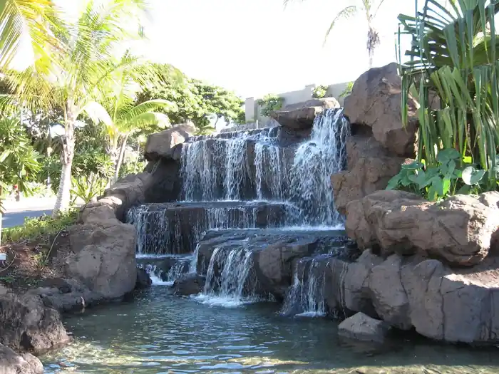 Tiered lava-rock waterfall spilling into a pool at the Ho'olei entry