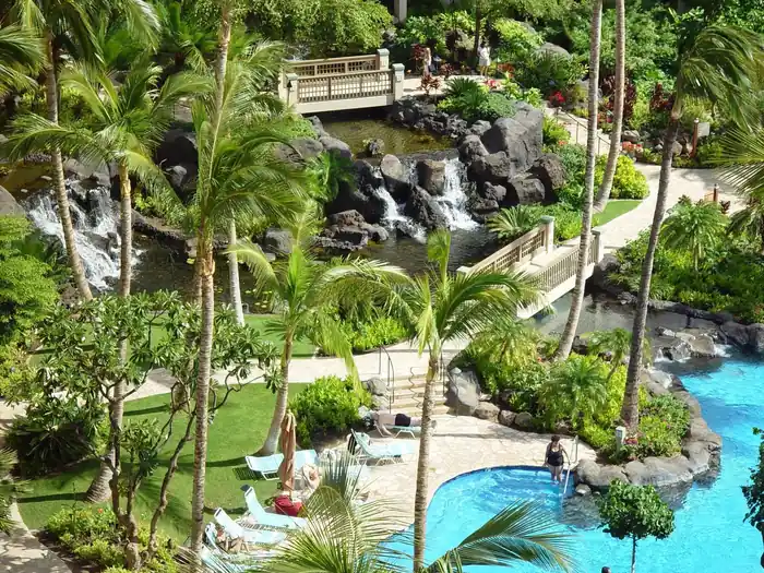 Lava-rock waterfalls and a stone footbridge beside a freeform lagoon pool, with palms and lawn around it