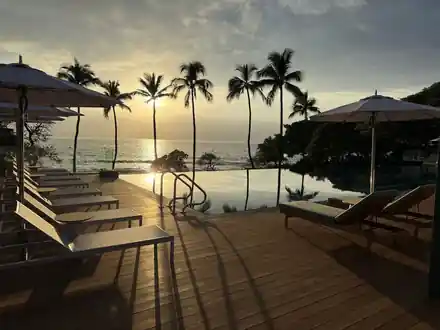 Infinity-edge pool deck at sunset with palms and the sun low on the ocean horizon