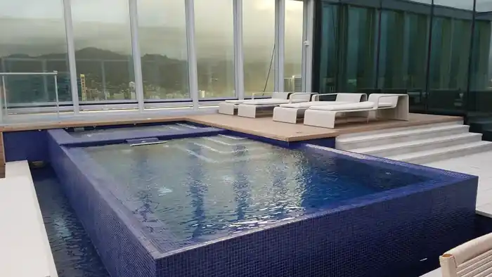 Raised spa in deep blue mosaic tile on a pool deck at Waiea, glass walls and hills behind