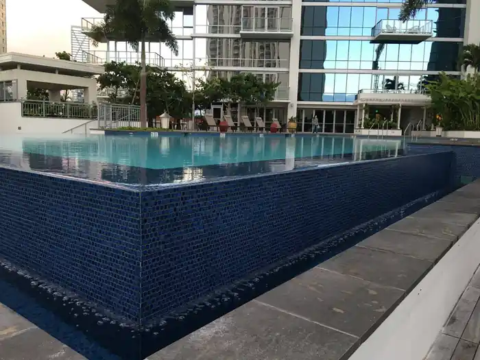 Waihonua rooftop pool with a dark-tiled spillover wall and city towers behind