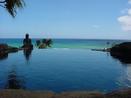 Infinity edge of dark water against turquoise sea with lava rock on both sides and a carved figure on the left rock